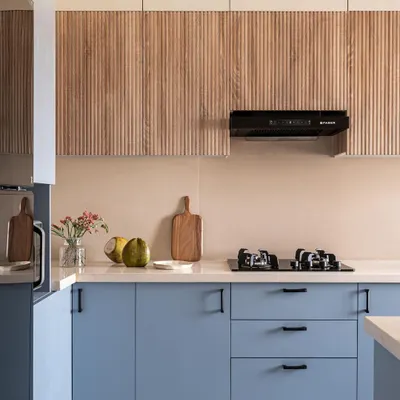 This two-tone modular kitchen combines periwinkle blue cabinets with textured wood-finish uppers. The design provides a clean, modern aesthetic with practical drawer systems and a durable countertop, perfect for a busy family.