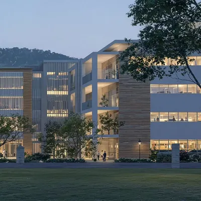 An evening render of the upcoming institute, focusing on the building's layered facade and open corner. The internal lighting transforms the building at night, revealing the activity within and highlighting the structural elegance of the open balconies and recessed spaces.