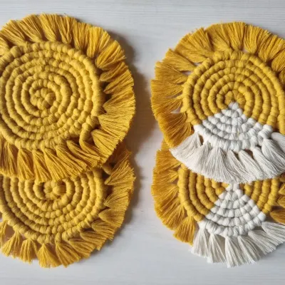 A set of my round, fringed macrame coasters in a sunny yellow. This image shows two design variations, one solid and one with a white accent, perfect for protecting your surfaces with style.