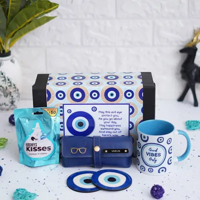 Send good vibes with this complete Evil Eye Hamper. It includes a themed ceramic mug, two matching tea coasters, a personalized eyewear case, and Hershey's chocolates, all packed in an evil eye themed box.