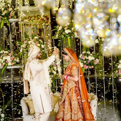The magical moment of the varmala exchange, framed by a stunning floral and crystal backdrop with confetti falling all around. This is a classic wedding shot captured with a sense of grandeur.