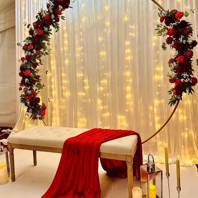 For a classic and passionate statement, you can’t go wrong with deep red roses. I designed this romantic backdrop with a full floral arch over a simple white bench, set against a curtain of warm fairy lights. This elegant stage decoration is perfect for making your engagement photos pop.