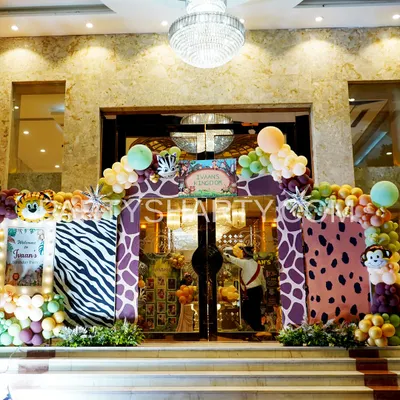 A grand jungle safari entrance featuring zebra and giraffe print arches, lush greenery, and a personalized 'Kingdom' sign for the birthday boy.