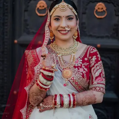 This bride looks absolutely regal in her red and white embroidered lehenga. Her makeup features a classic red lip and defined eyes, a timeless combination that perfectly complements her traditional bridal jewelry and the grandeur of her outfit.
