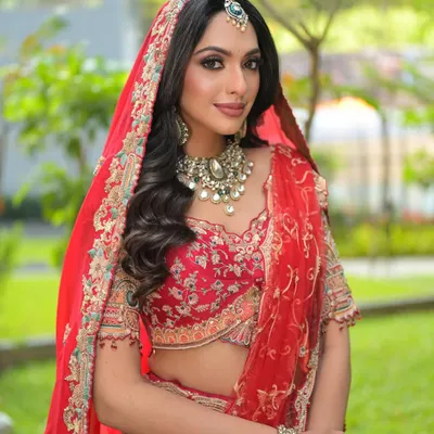 A full-length view of my signature red bridal lehenga look. The makeup is designed to be radiant in natural light, with soft, wavy hair and a perfectly draped dupatta creating a look of timeless elegance.