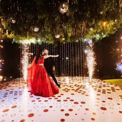 The perfect dance pose, captured forever. The bride's stunning red lehenga flows beautifully as they perform their choreographed first dance, framed by sparklers and elegant decor.
