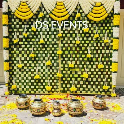 An eco-friendly backdrop crafted from intricately woven coconut leaves (thenga olai). The hanging marigold and tuberose garlands add a touch of color and fragrance, perfect for a traditional pooja or ceremony.