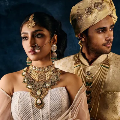 A classic couple portrait from a bridal jewellery campaign. The lighting is carefully balanced to illuminate the bride's layered necklace and maang tikka, as well as the groom's complementary jewels, creating a cohesive and luxurious look.