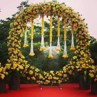 A beautiful circular floral arch made of yellow marigolds, perfect for a Haldi ceremony. The hanging floral strings add a traditional and elegant touch to the decor.