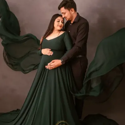 An intimate couple's portrait in our studio. The partner embraces the mother-to-be from behind, both gently holding the baby bump, surrounded by flowing green fabric.