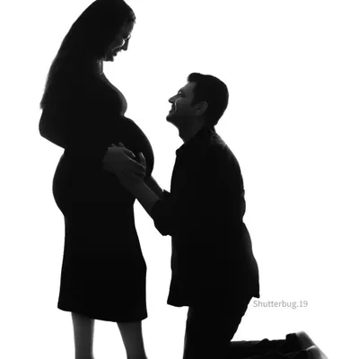 A powerful and artistic silhouette of an expecting couple. The father-to-be kneels in adoration of his partner and their coming child, creating a deeply emotional and visually striking image.