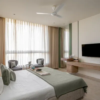 A full view of a master bedroom I furnished in a Thane apartment. I built the bed with its faux leather headboard, the floating media unit, and the small seating area with two chairs, creating a complete and cohesive look.