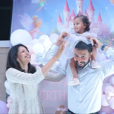 The pure joy of a birthday party! A father lifts his daughter onto his shoulders against a festive fairy-themed backdrop.
