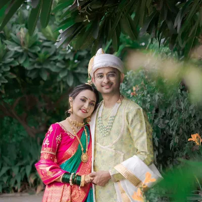 A lovely portrait of a Maharashtrian couple, their colorful traditional attire vibrant against the lush green background of their outdoor wedding.