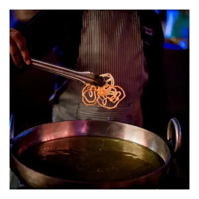 A chef carefully lifts a freshly fried, crispy nano jalebi from the hot oil. Our live jalebi station is a sensory delight, filling the air with a sweet aroma and serving this Indian classic at its absolute best.