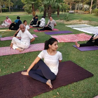 A participant holds a spinal twist during our International Yoga Day 2019 celebration in a Noida park. You can see people of all ages practicing together in the background.