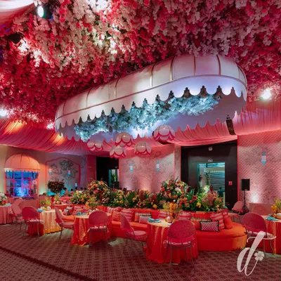 The evening look of our 'La Dolce Vita' theme, where the space was transformed with dramatic pink lighting. A custom canopy filled with blue hydrangeas became a central feature, surrounded by plush orange seating and tables set for a luxurious dinner.