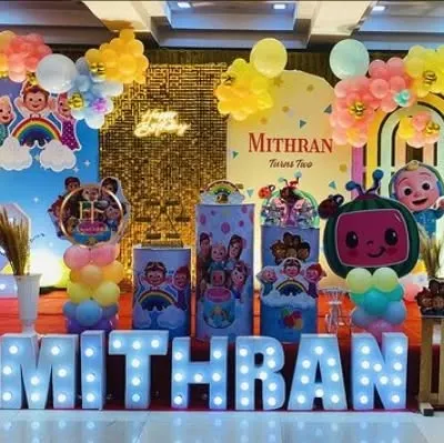 A vibrant Cocomelon themed birthday party with a large backdrop, character cutouts, and a shimmer wall for extra sparkle.
