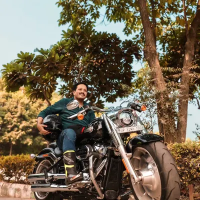 A portrait of a rider on his Harley Davidson Fat Boy. The low angle emphasizes the bike's powerful presence, while the natural, leafy background provides a great contrast to the chrome and black metal.