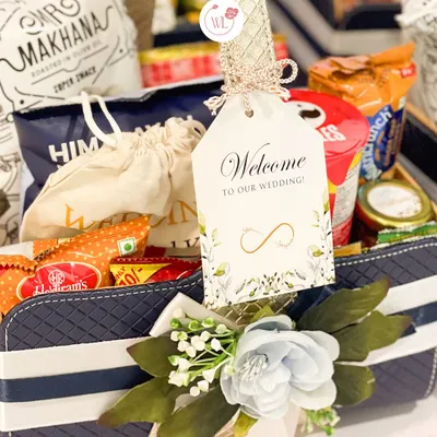A close-up of our welcome room hamper, featuring a personalized "Welcome to our wedding!" tag, a mix of popular Indian snacks, and a touch of floral decoration.