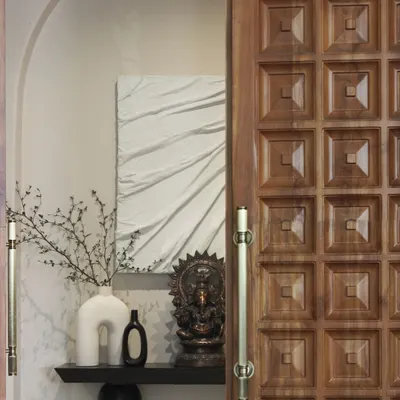 The entryway of the Jaipur House features a traditionally carved teakwood door. It opens to reveal a carefully composed scene with textile art and curated objects, setting a narrative tone for the entire home.