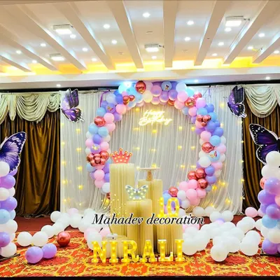 A stunning butterfly theme birthday party in a large hall. This setup features a circular balloon arch in pastel colors against a white curtain backdrop, with large purple butterfly cutouts on balloon pillars.