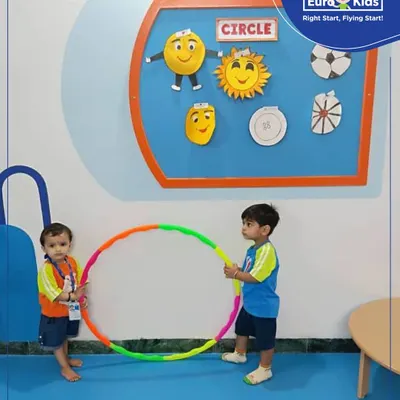 Two toddlers work together holding a large hula hoop, learning about circles and collaboration during our "Circle Day" activity.