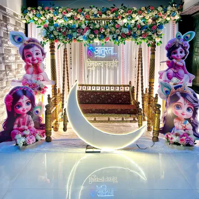 This 'Radha or Krishna' themed baby shower stage combines a traditional wooden swing and floral canopy with a modern LED moon prop. The neon sign in Marathi adds a personal touch to the backdrop.