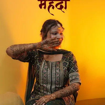 A shy smile and the beautiful fragrance of henna. This is a classic bridal portrait from a Mehendi ceremony, using warm lighting to highlight the bride's glow and the intricate henna design she's hiding with a playful hand.