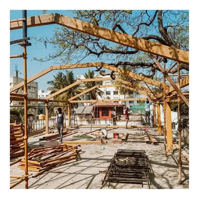 The initial construction phase of the rooftop conservatory, showing the assembly of the wooden frame under a large rain-tree. This image captures the raw beginning, where the architectural vision starts to take physical form.