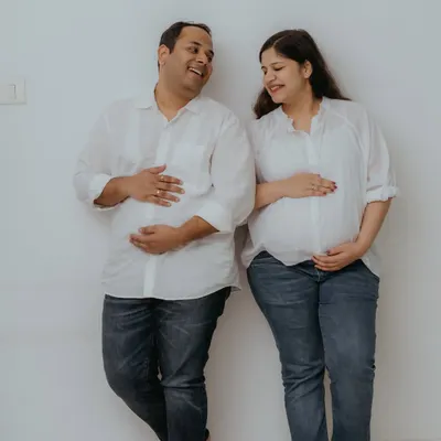 A fun and playful moment from a lifestyle home session, with both parents-to-be cradling their bellies. Dressed in matching casual white shirts and jeans, their shared laughter makes for a perfectly relaxed and joyful couple's maternity photo.