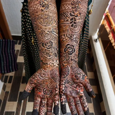 A stunning full-coverage bridal mehendi with a mix of floral and geometric patterns. Notice how the dark, filled-in flowers pop against the lighter, detailed background.
