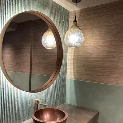In this powder room, a palette of soft greens and browns creates a calming effect. The ribbed texture of the tiles, a hammered copper sink, and a mercury glass pendant light come together to form a space that is rich in texture.