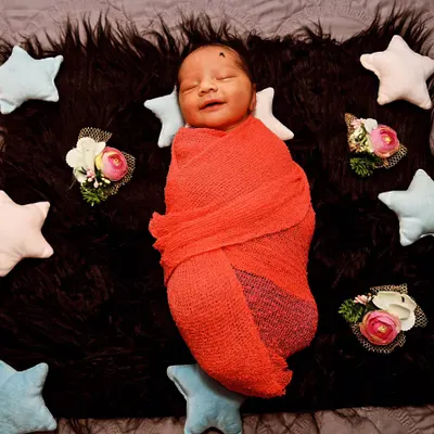 The sweetest smile from a sleeping baby, snugly wrapped in a red knit on a dark, furry blanket. The contrast makes the moment pop.