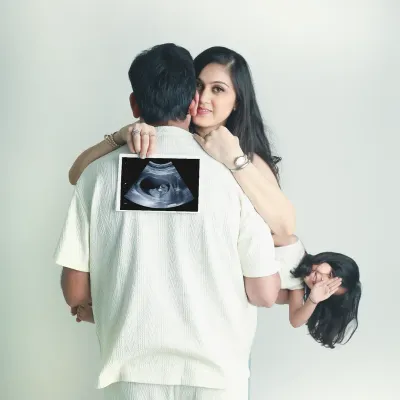 A creative and heartwarming pregnancy announcement. The family comes together to showcase the sonogram, with the older sibling peeking out playfully.