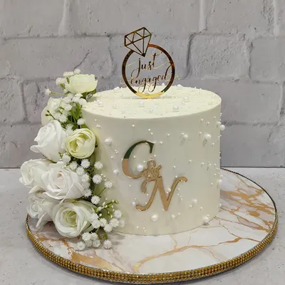 A classic and timeless engagement cake. This design features a clean white finish, a cascade of white roses, delicate pearl details, and a custom gold monogram for the happy couple.