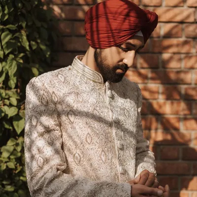 A groom adjusts his cuff, captured in warm sunlight against a brick wall. This is a classic, stylish portrait.