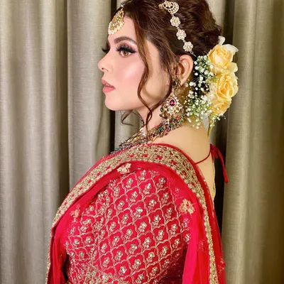 A beautiful side profile showcasing an elegant bridal updo adorned with fresh yellow roses. This hairstyle perfectly complements the traditional red lehenga.