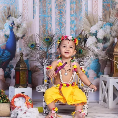 A joyful Little Krishna, smiling brightly while seated on a miniature throne adorned with peacock feathers. This setup is perfect for capturing your baby's happy spirit during Janmashtami.