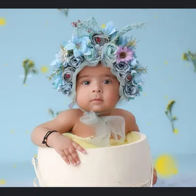 This little one looks so curious, peeking out of a white bucket while wearing an intricate blue floral bonnet. Sitter sessions are perfect for capturing these inquisitive and adorable expressions.