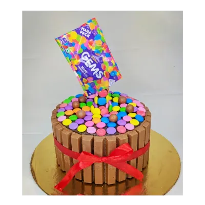 An anti-gravity Gems explosion cake that's as fun to look at as it is to eat. This is a chocolate truffle cake surrounded by KitKat bars, with colorful Gems pouring out of the bag.
