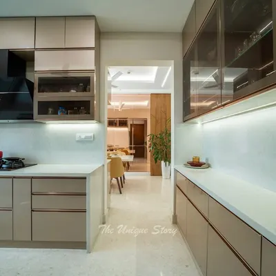 This modern kitchen is designed for a clean and calm aesthetic, featuring glossy, handle-less beige cabinets and a white quartz countertop. The view opens into the dining area, showcasing the open-concept layout that connects the spaces.