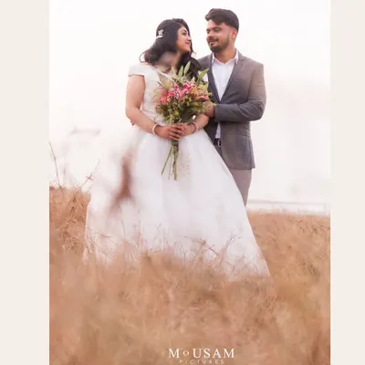 A classic, romantic portrait in a field of golden grass. She holds a bouquet as he stands beside her, their gazes meeting in a moment of sweet connection. The soft light creates a dreamy, fairytale atmosphere.
