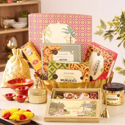 This grand festive hamper is a true celebration, overflowing with boxes of Anand methi mathi and murukku, a jar of badamika, and a selection of sweets, all beautifully arranged in a large, ornate basket.