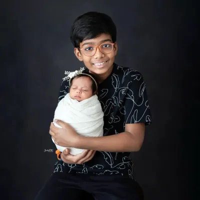 A proud big brother holding his newborn sister. I use a simple, dark background to create a classic and timeless sibling portrait that focuses on their bond.