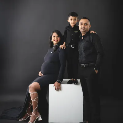 A fun and stylish family portrait in matching black outfits. The older brother stands proudly on a block, excited about his promotion.