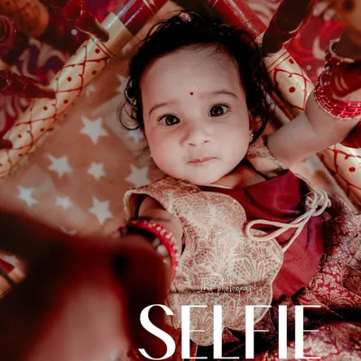 A creative and cute shot of a baby in a traditional cradle during her naming ceremony. The unique angle and "Selfie" text overlay add a modern, playful touch to this traditional event photo.