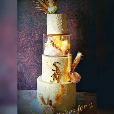A beautiful four-tier wedding cake with a rustic, bohemian theme. The design features textured buttercream, dried pampas grass, and the couple's initials for a personal touch.