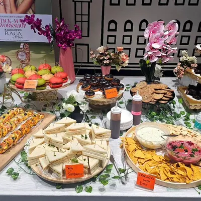 A full view of our stunning hi-tea grazing table set up for a workshop at a Bangalore shopping mall. It features an abundant spread of sandwiches, macarons, donuts, nachos with dip, and more.