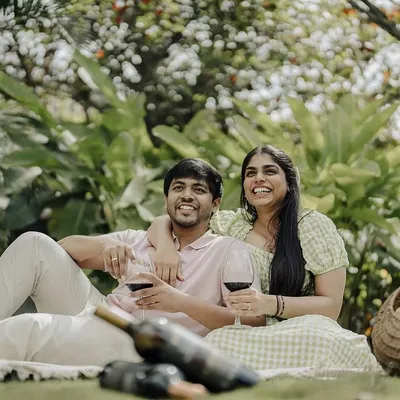 A relaxed and happy pre-wedding picnic. This shot captures the couple enjoying a glass of wine and each other's company in a beautiful, natural setting, showcasing their easygoing connection.